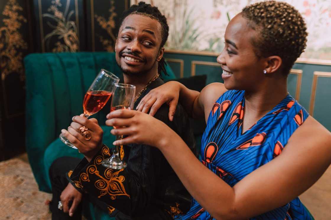 A man and a woman sit close together on a sofa, smiling and holding drinks. A man and a woman sit close together on a sofa, smiling and holding drinks.