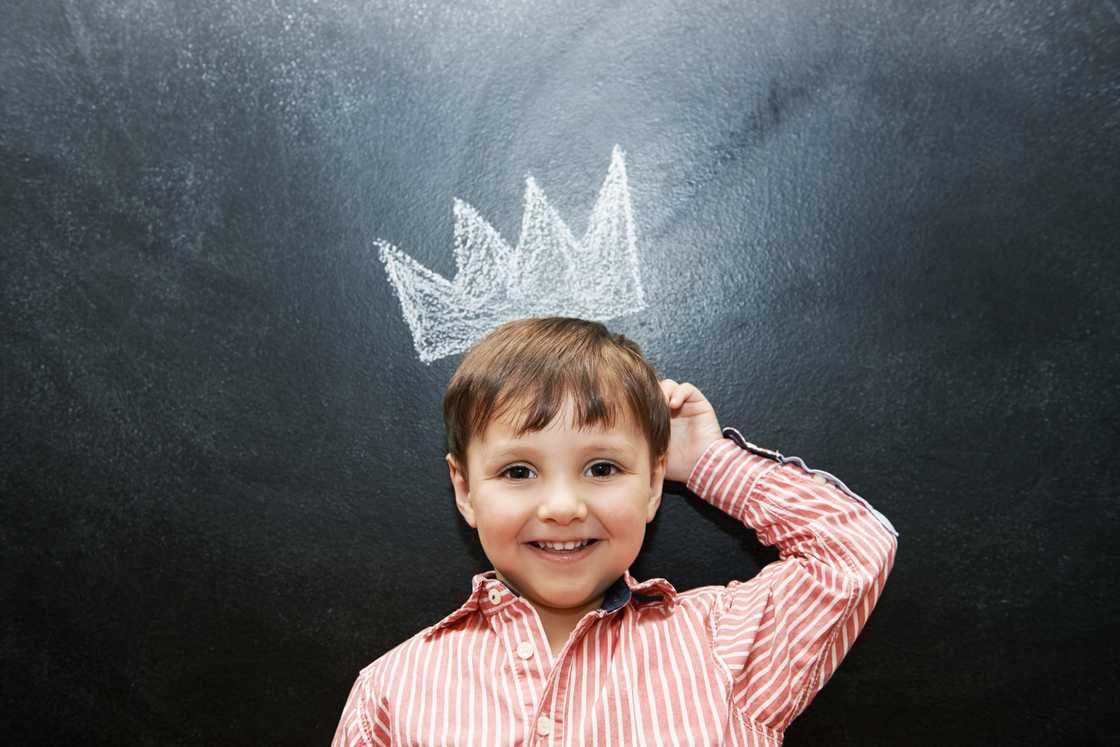 A boy is standing next to a blackboard with a crown drawing. A boy is standing next to a blackboard with a crown drawing.