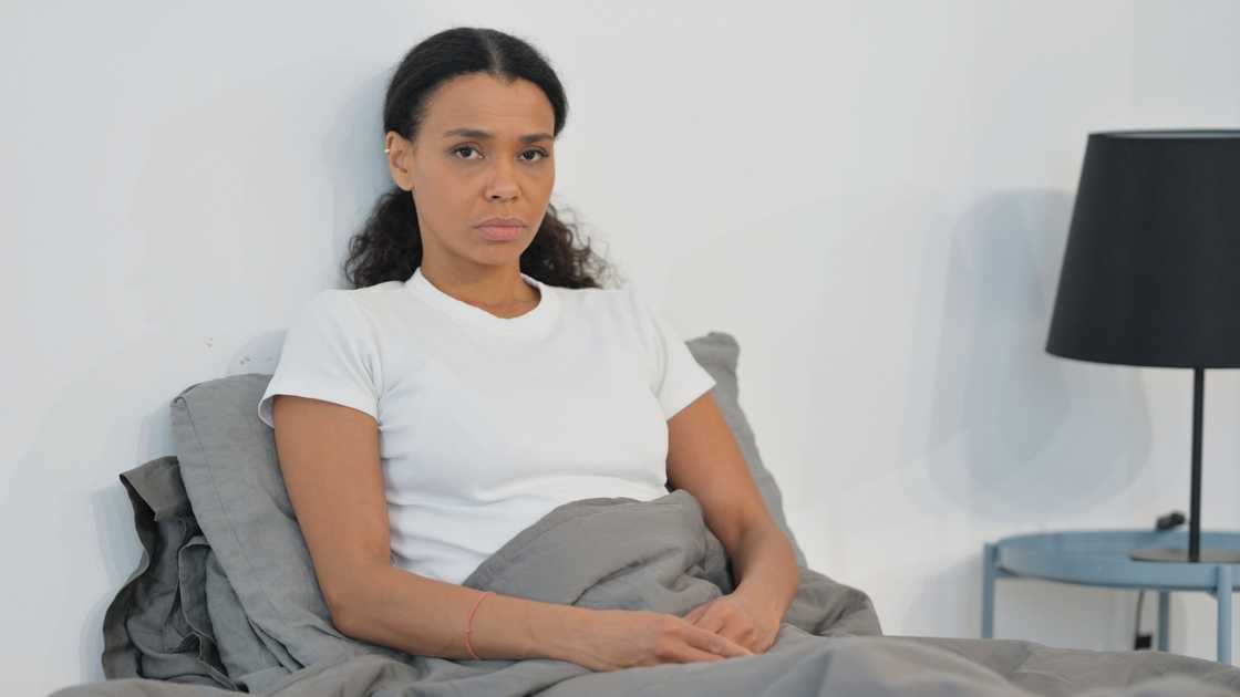 A serious woman sitting on bed thinking