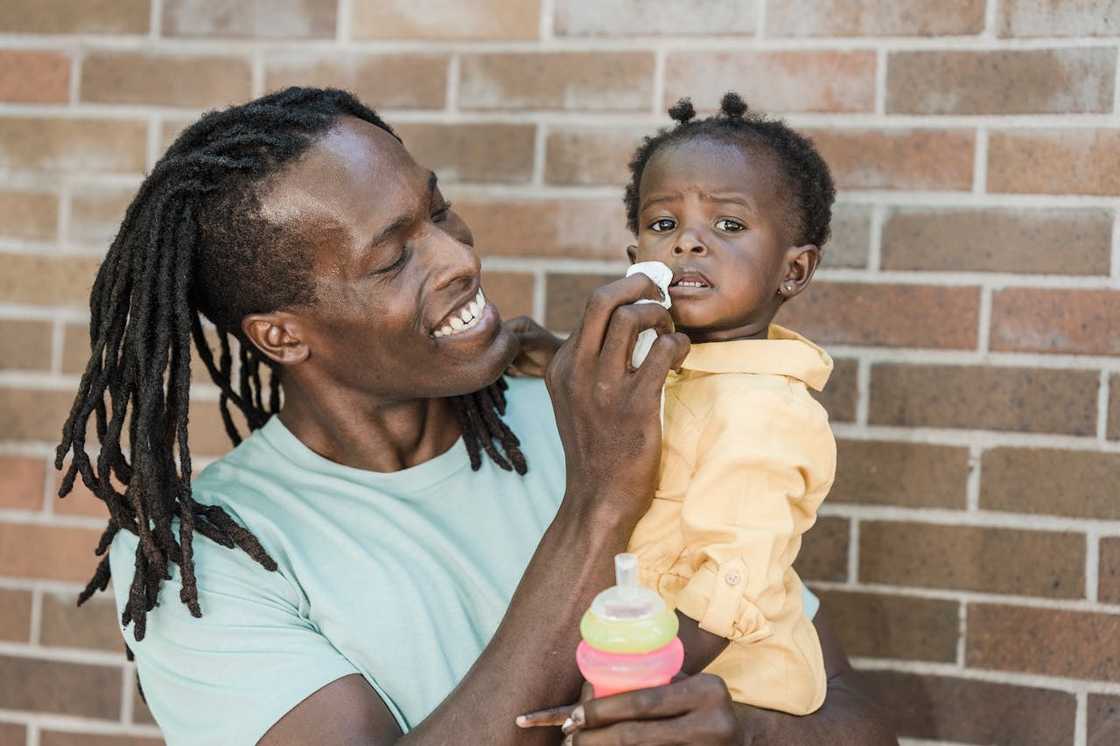An adult wipes a toddler’s face while holding the child.