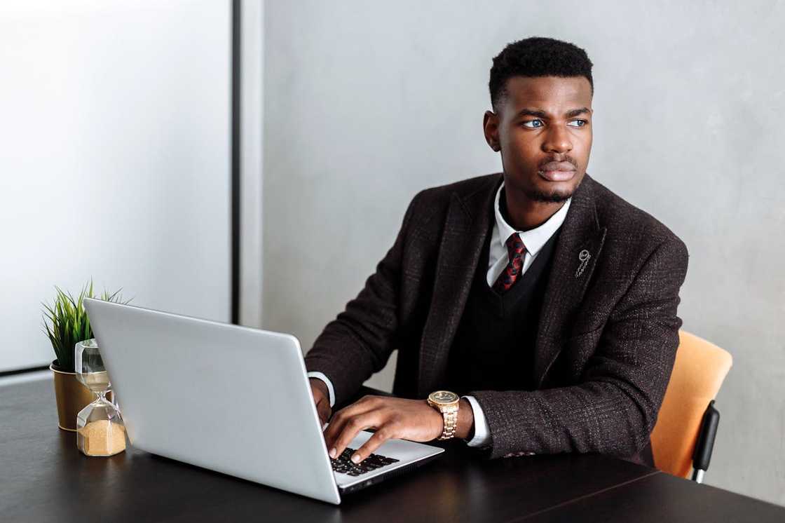 A professional-looking man sits at a desk using a laptop.