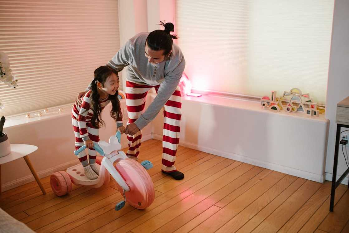 Girl on a tricycle assisted by her father