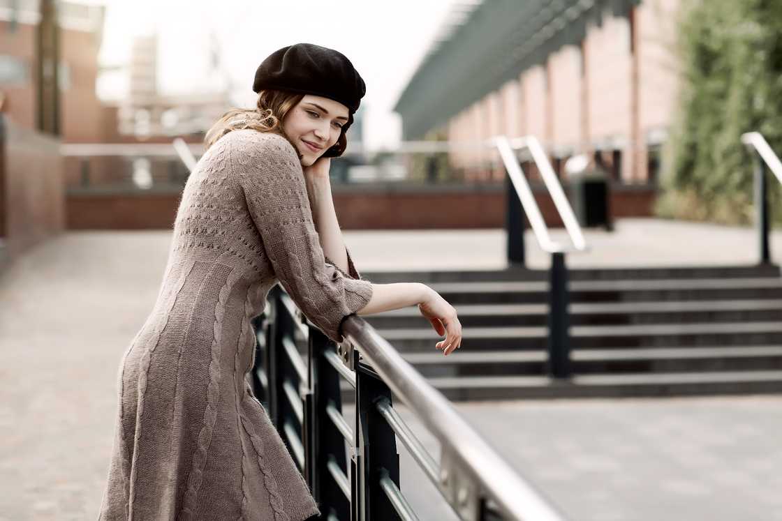 Portrait of a young woman wearing a beret and knitted dress leaning on a railing Portrait of a young woman wearing a beret and knitted dress leaning on a railing