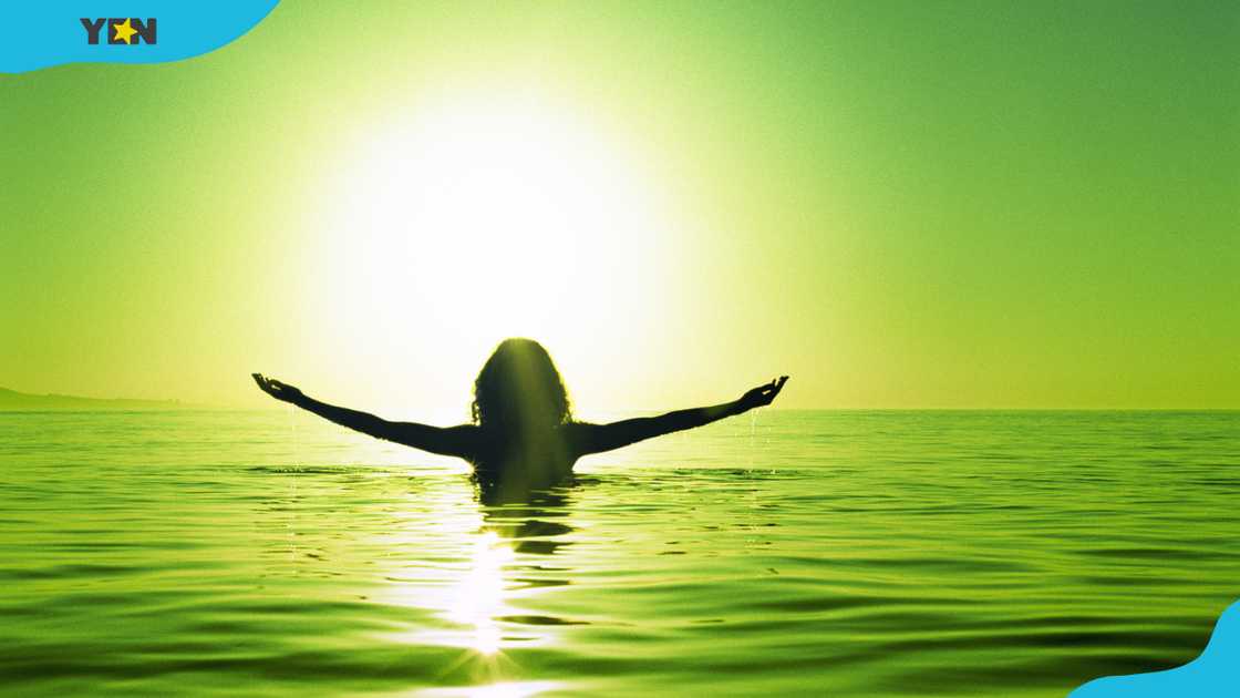Woman in sea, arms outstretched, rear view with green background