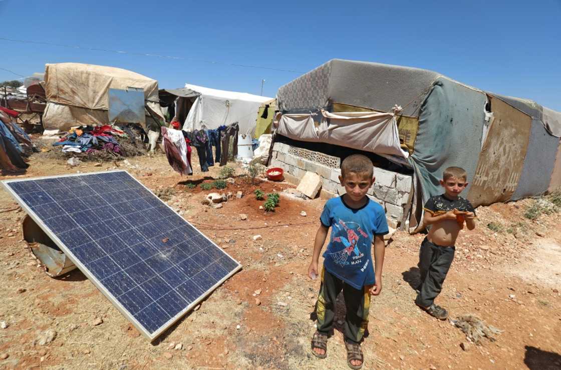 Children stand near a solar panel at a camp for Syrians displaced by conflict, near the Syrian border with Turkey in the rebel-held northern part of Idlib province Children stand near a solar panel at a camp for Syrians displaced by conflict, near the Syrian border with Turkey in the rebel-held northern part of Idlib province