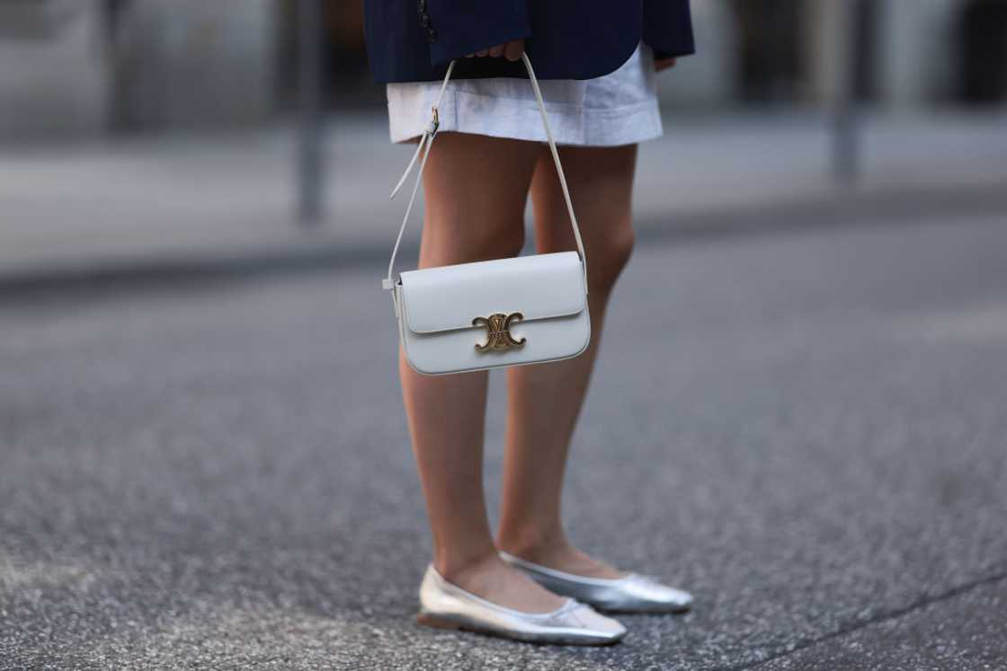 A woman in a white skirt and blazer holds a small white Celine purse.