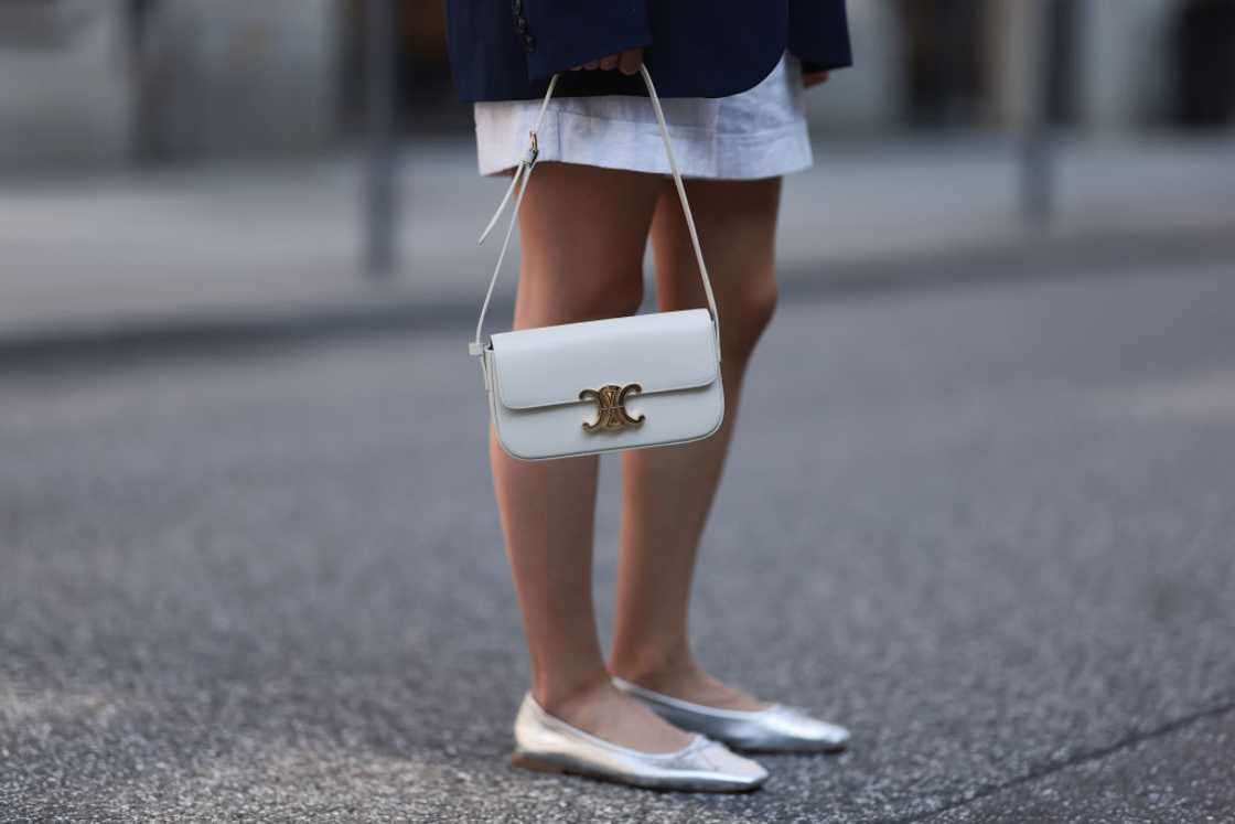 A woman in a white skirt and blazer holds a small white Celine purse. A woman in a white skirt and blazer holds a small white Celine purse.