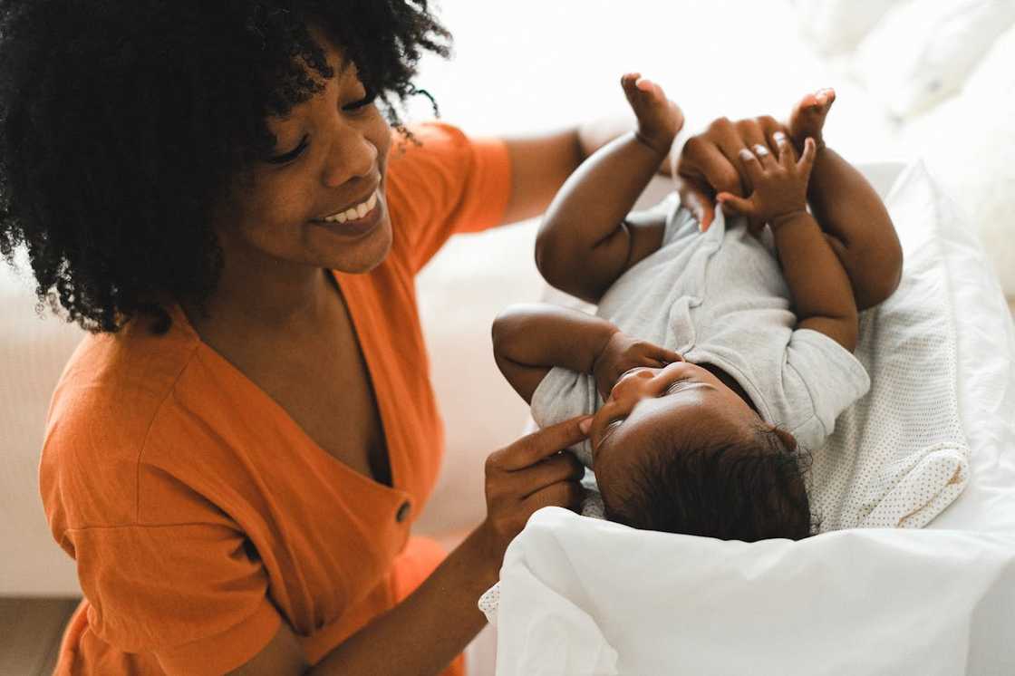 A woman smiles while changing a baby on a padded surface. A woman smiles while changing a baby on a padded surface.