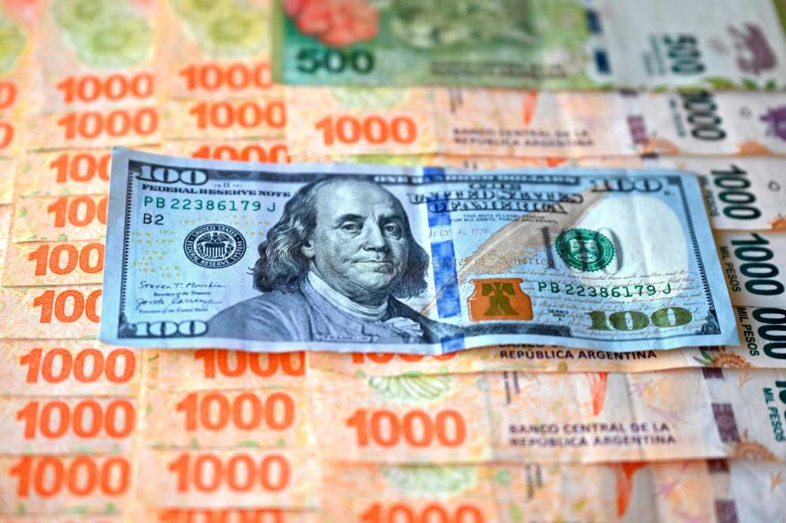(FILES) This illustration shows a US $100 banknote on top of Argentine pesos (FILES) This illustration shows a US $100 banknote on top of Argentine pesos