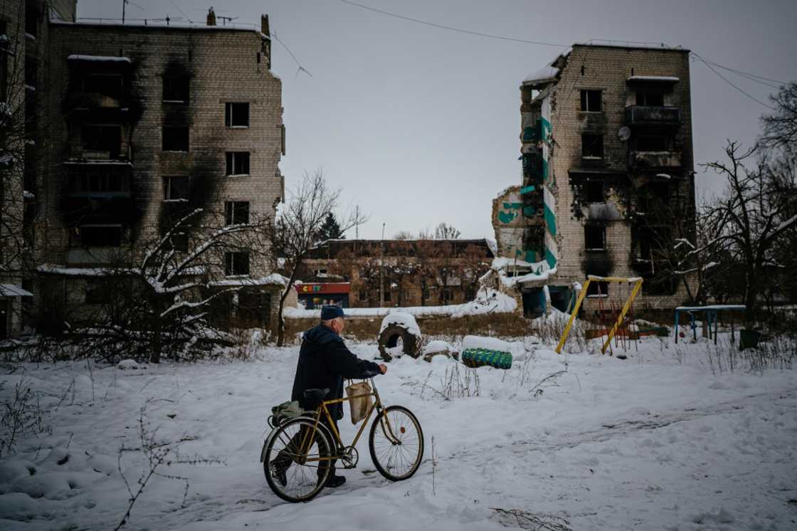 A resident of Borodianka pushes his bike on a snow covered street next to destroyed residential buildings A resident of Borodianka pushes his bike on a snow covered street next to destroyed residential buildings