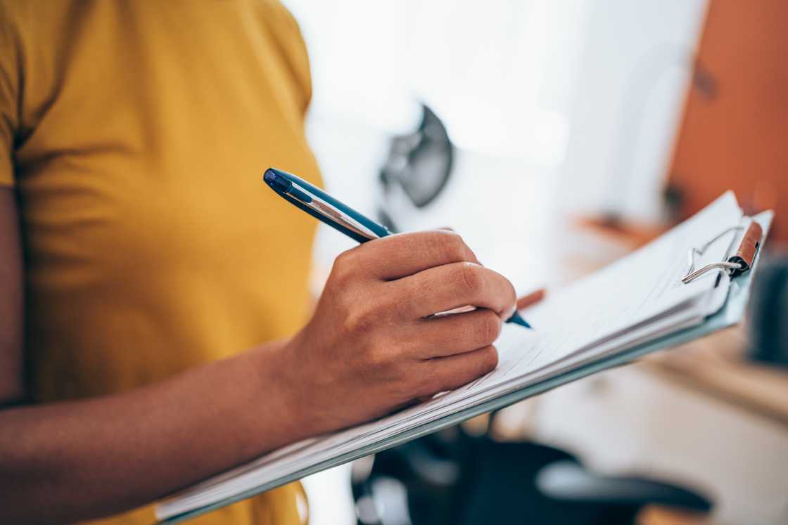 A woman handwriting on clipboard with a pen A woman handwriting on clipboard with a pen