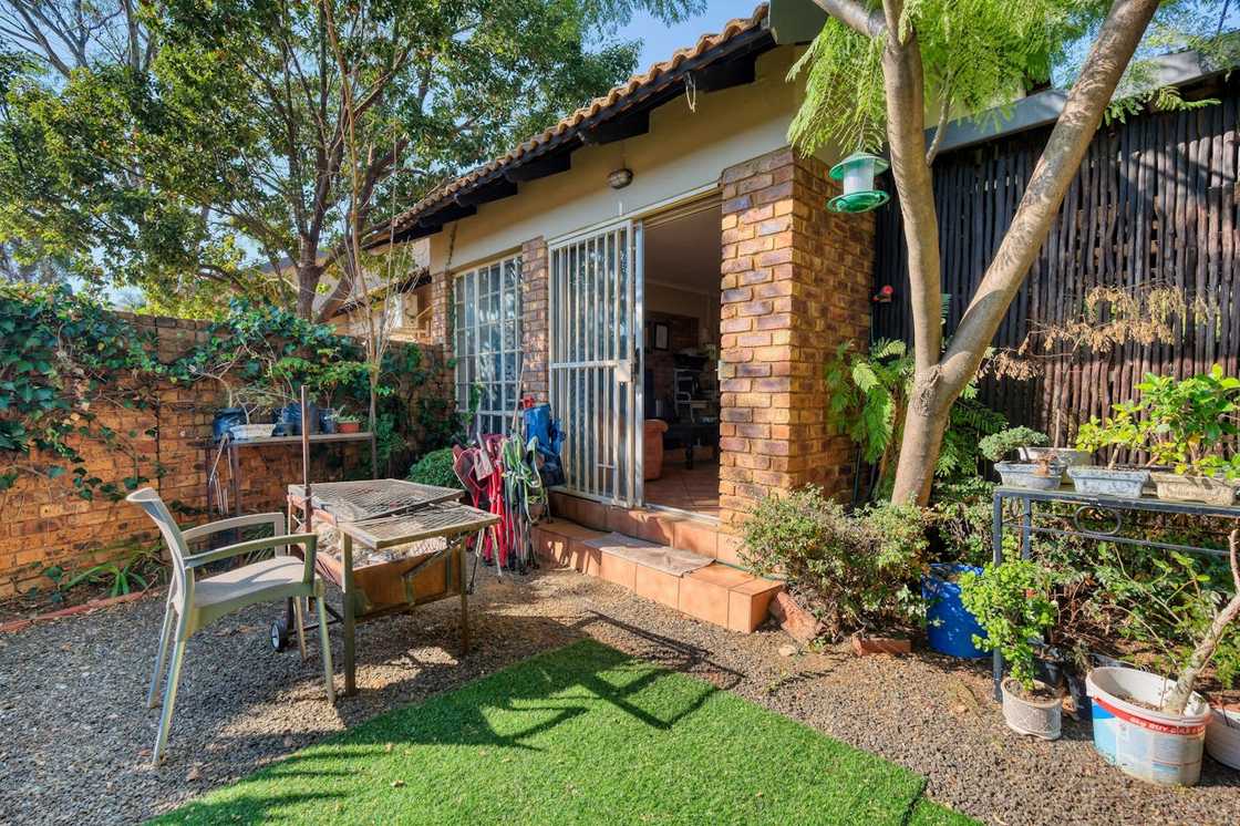 A small house sits in a quiet yard with garden tools outside.