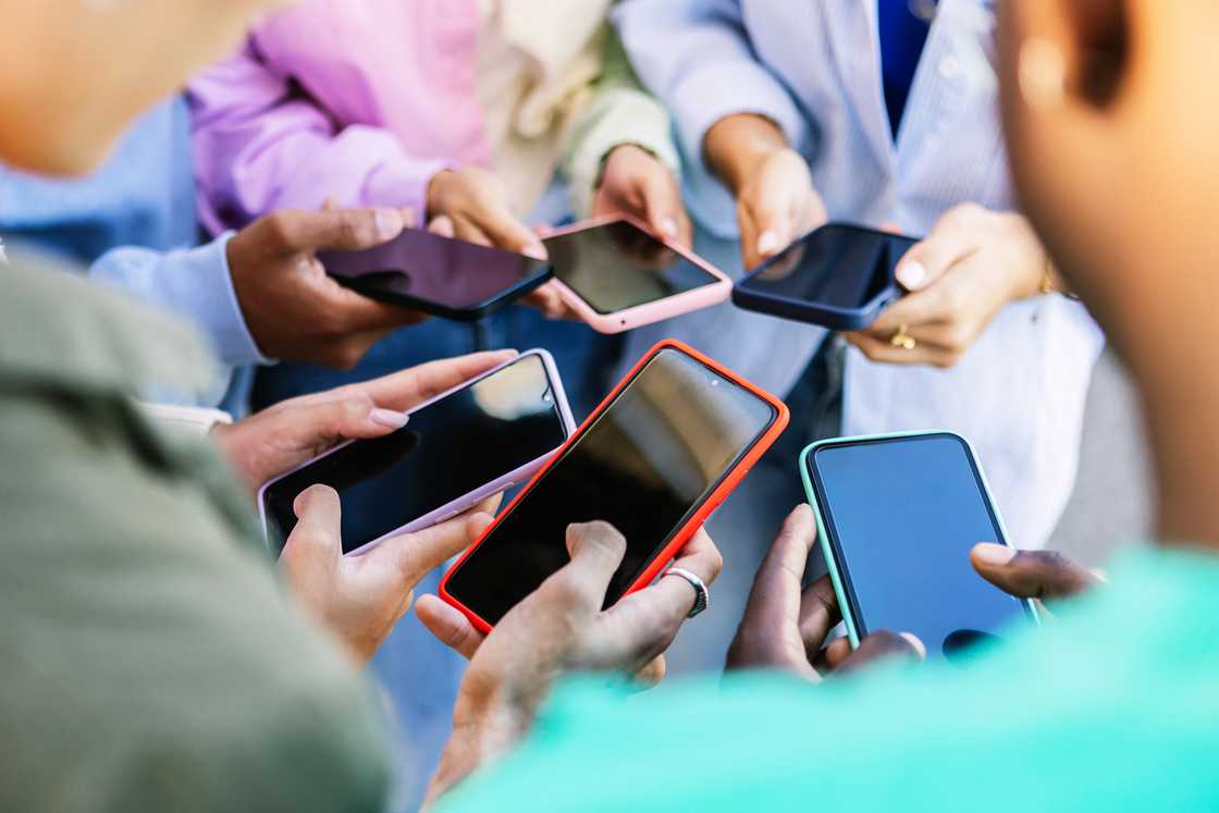 A group of people standing in a circle while holding their phones.