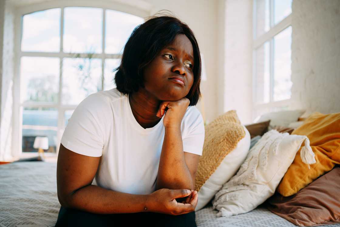A woman sits sad and upset in the bedroom.