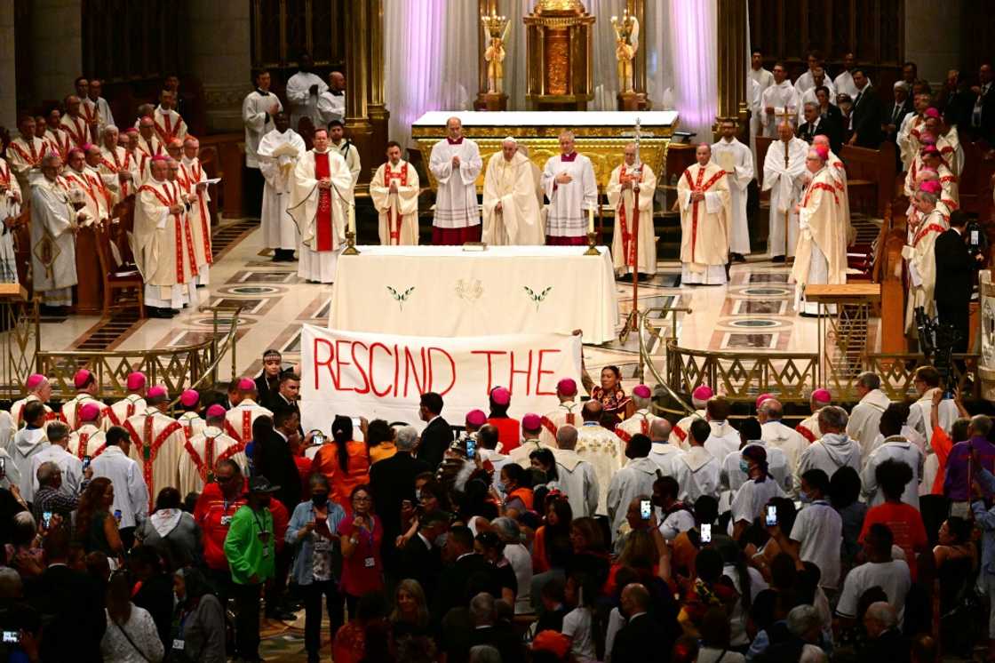 Indigenous people hold a protest banner as Pope Francis celebrates mass at the shrine of Sainte-Anne-de-Beaupre in Quebec, Canada, on July 28, 2022 Indigenous people hold a protest banner as Pope Francis celebrates mass at the shrine of Sainte-Anne-de-Beaupre in Quebec, Canada, on July 28, 2022
