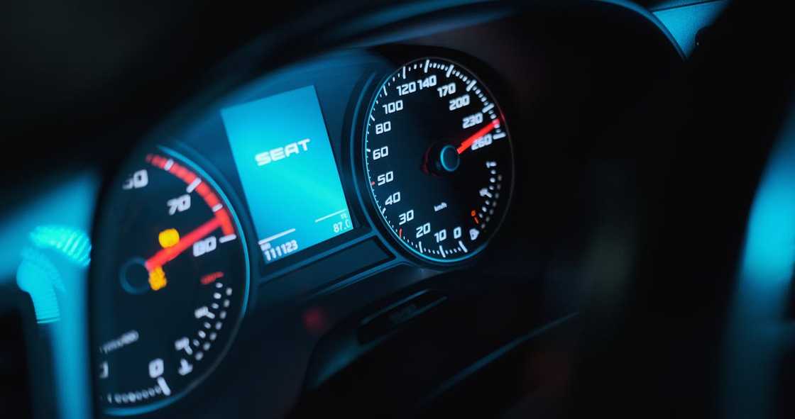 A car dashboard shows a speedometer illuminated in the dark.