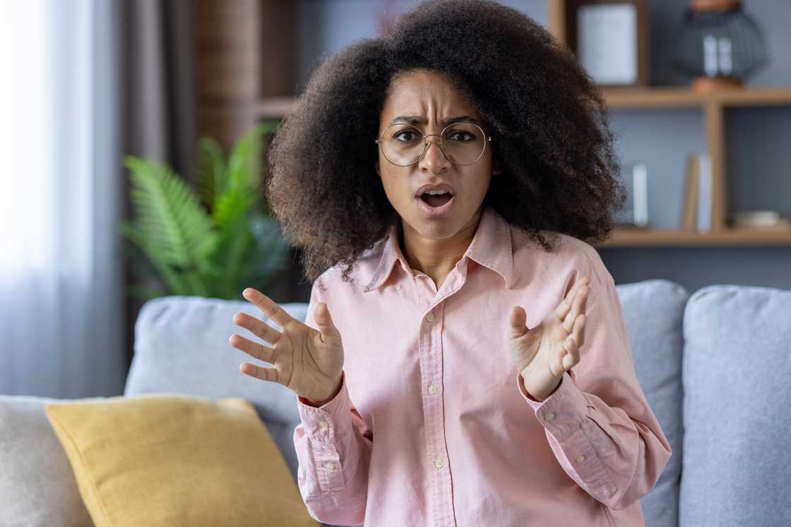 Surprised woman with curly hair and glasses sitting on a couch at home Surprised woman with curly hair and glasses sitting on a couch at home