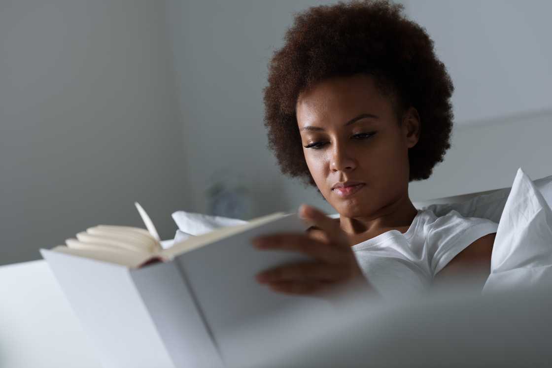 A young woman lying in bed reading a book A young woman lying in bed reading a book