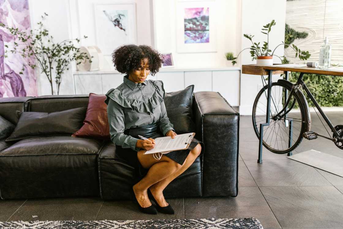 A woman sitting on leather sofa while signing documents A woman sitting on leather sofa while signing documents