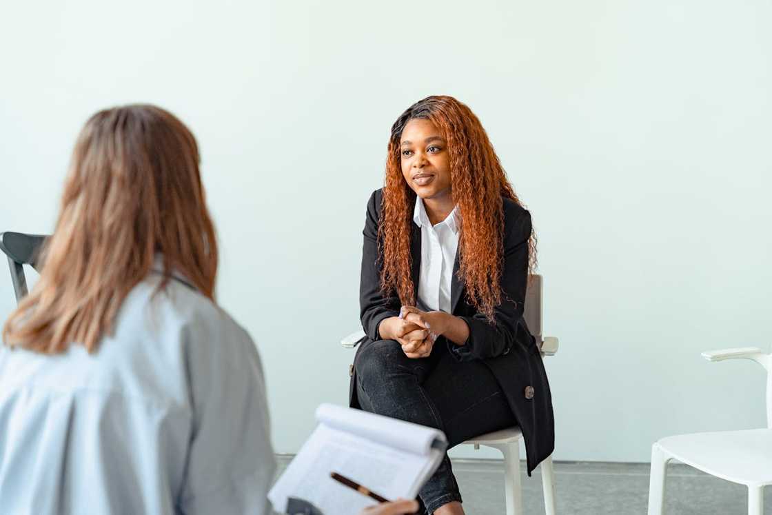 A woman seated in a chair, listening attentively during an interview session. A woman seated in a chair, listening attentively during an interview session.