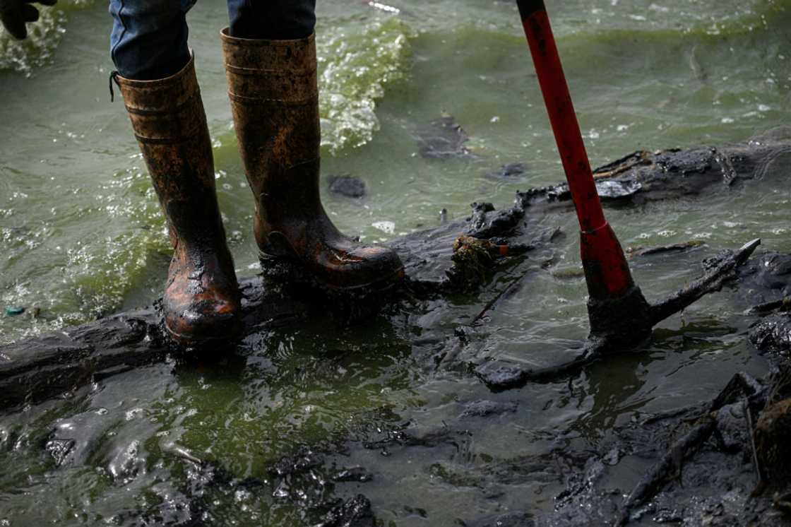 A fisherman with boots covered in oil stands on a contaminated shore of Lake Maracaibo in Venezuela, on July 11, 2024