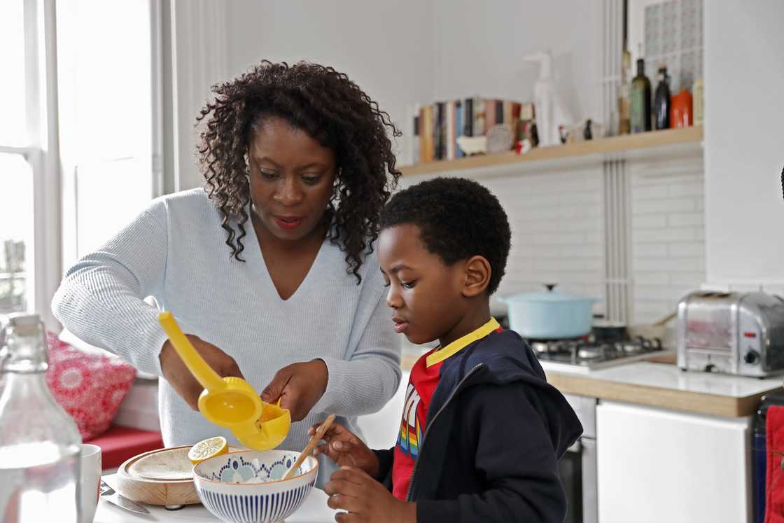 Mother helping a young boy in the kitchen with cooking Mother helping a young boy in the kitchen with cooking