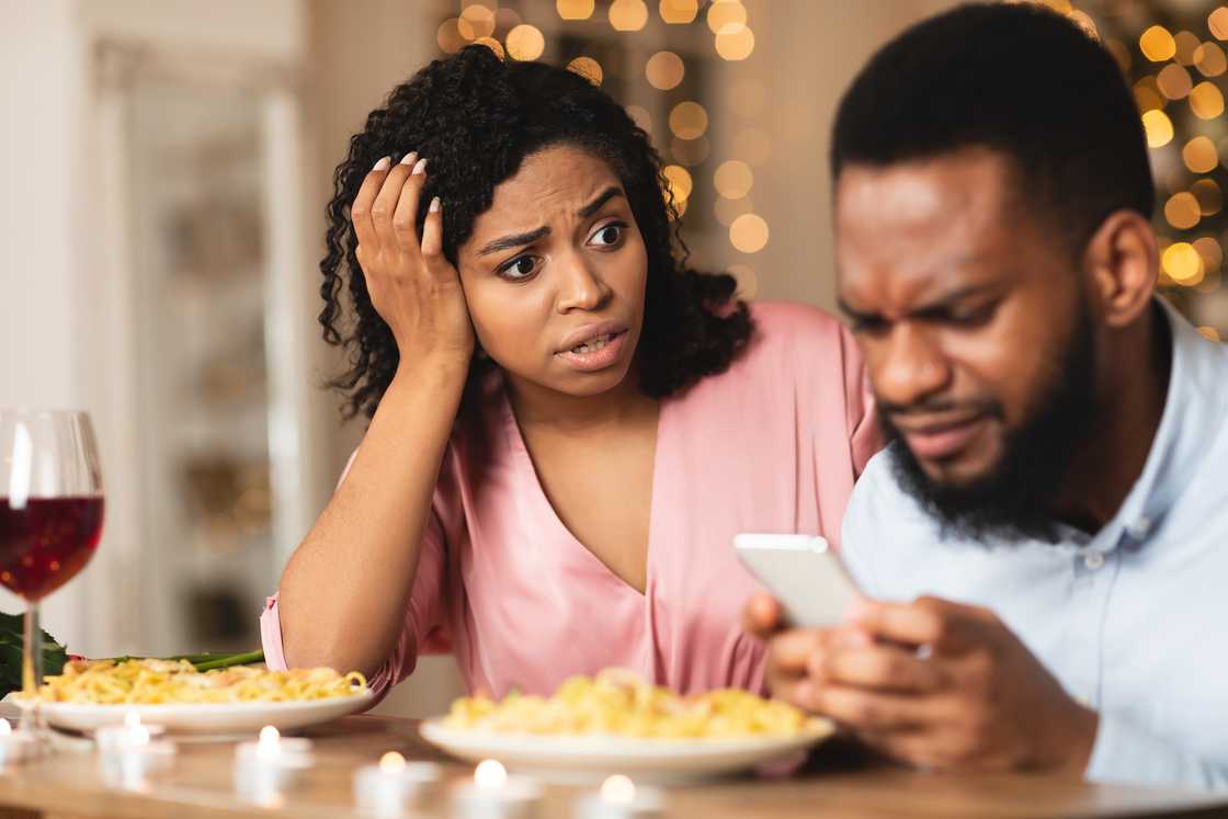 An angry woman looking at her boyfriend stuck on his smartphone. An angry woman looking at her boyfriend stuck on his smartphone.