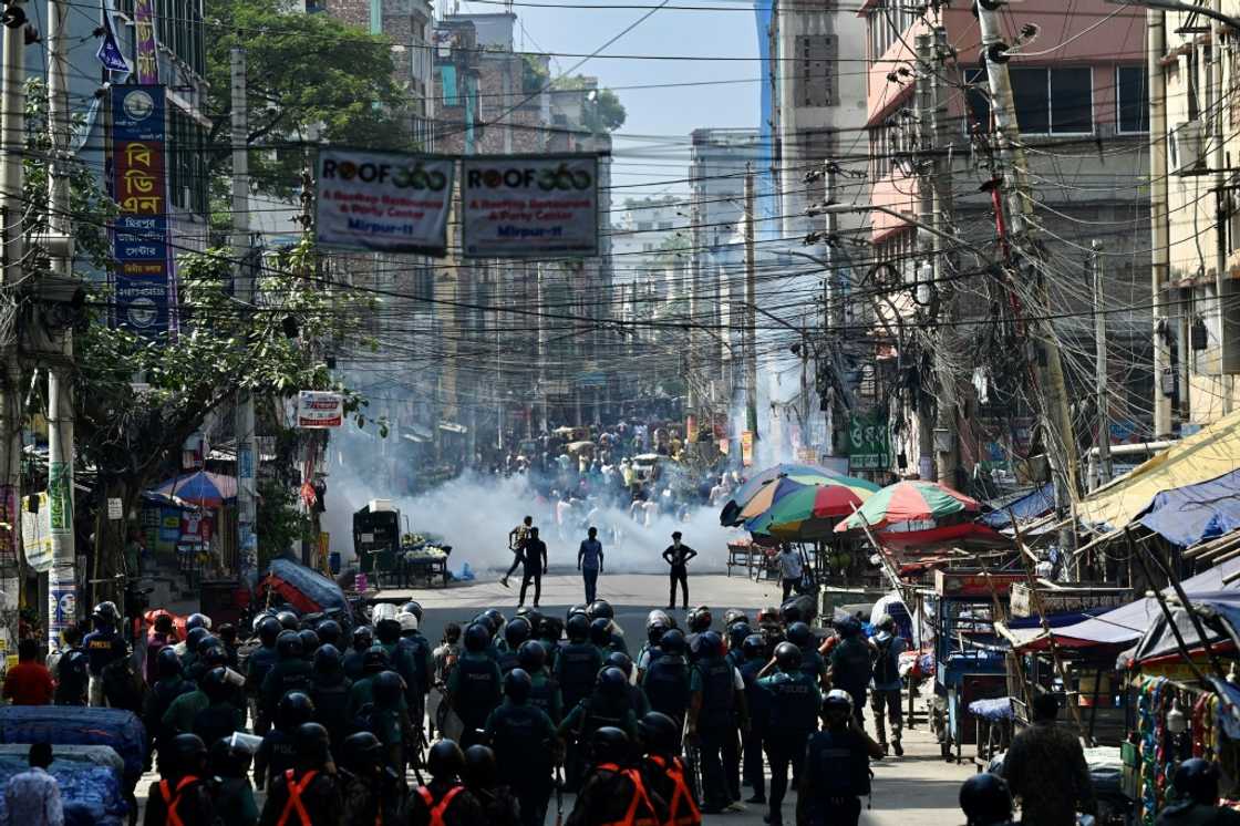 Bangladesh police (foreground) stand guard clashes with garment workers (top)demanding higher wages Bangladesh police (foreground) stand guard clashes with garment workers (top)demanding higher wages