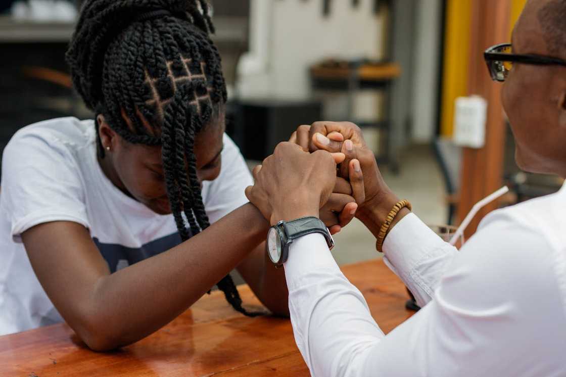 Two people sit at a table holding hands in a moment of emotional support.