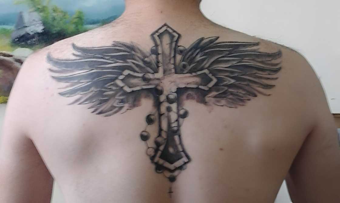 A man has a cross with wings tattoo on his upper back A man has a cross with wings tattoo on his upper back