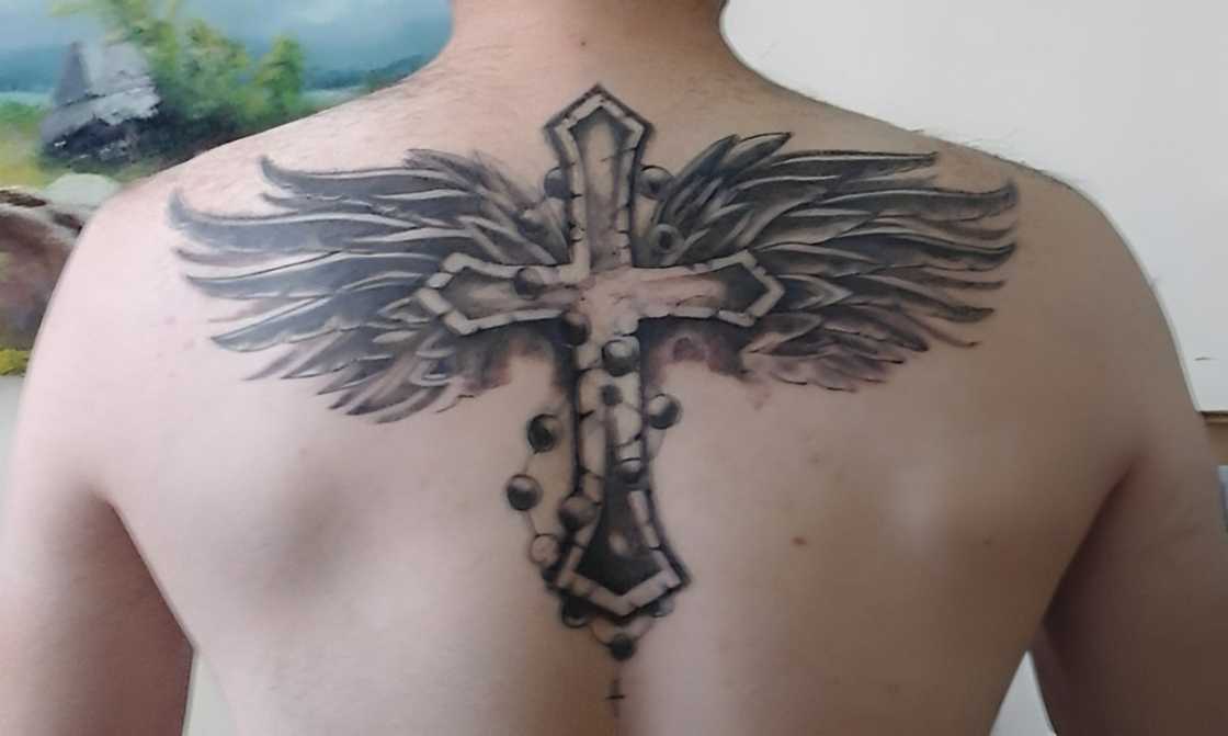 A man has a cross with wings tattoo on his upper back