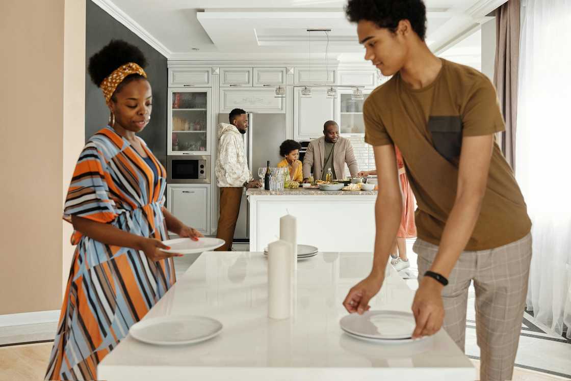 A young man helps his mom set the dinner table.