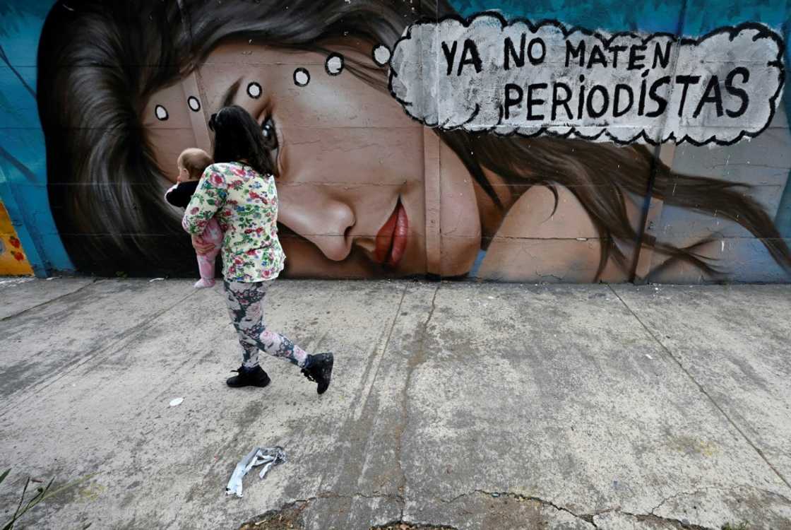 A woman holding a baby walks past a mural reading 'Stop killing journalists' in Mexico City A woman holding a baby walks past a mural reading 'Stop killing journalists' in Mexico City