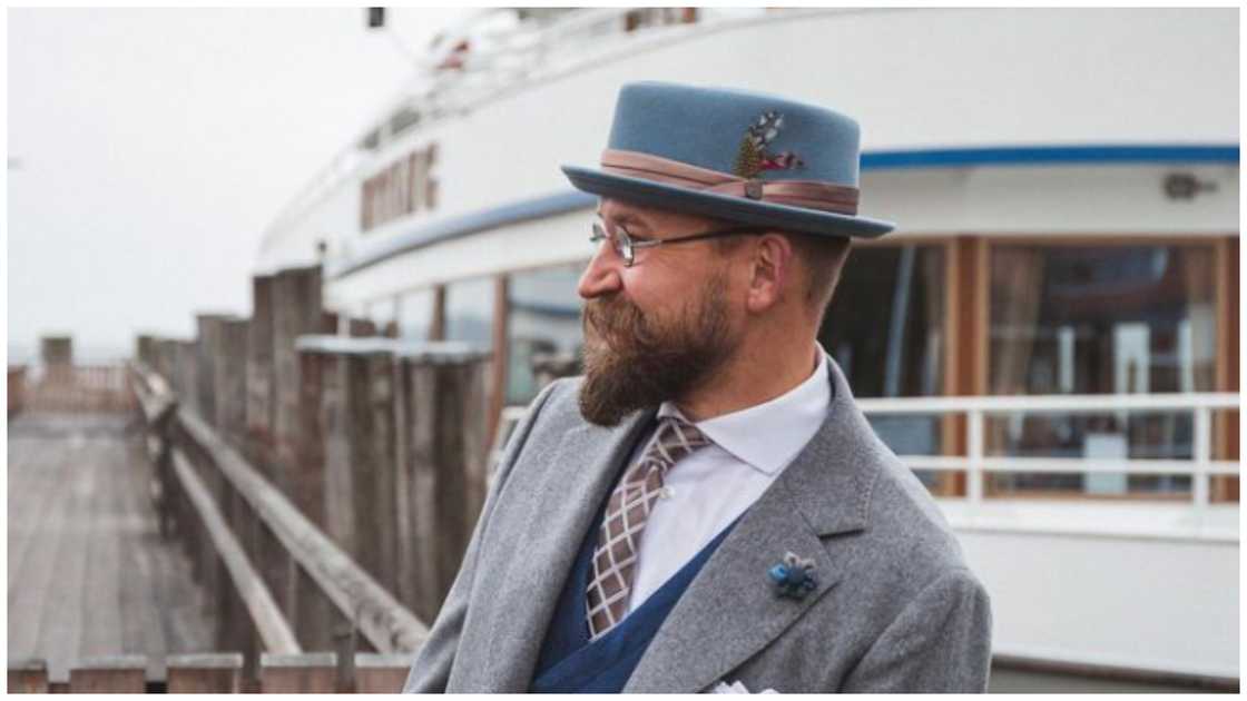 A man is standing next to yacht wearing a blue pork pie hat A man is standing next to yacht wearing a blue pork pie hat