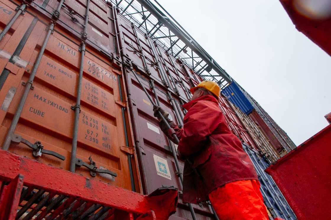 A port worker securing stacked shipping containers at a cargo terminal. A port worker securing stacked shipping containers at a cargo terminal.