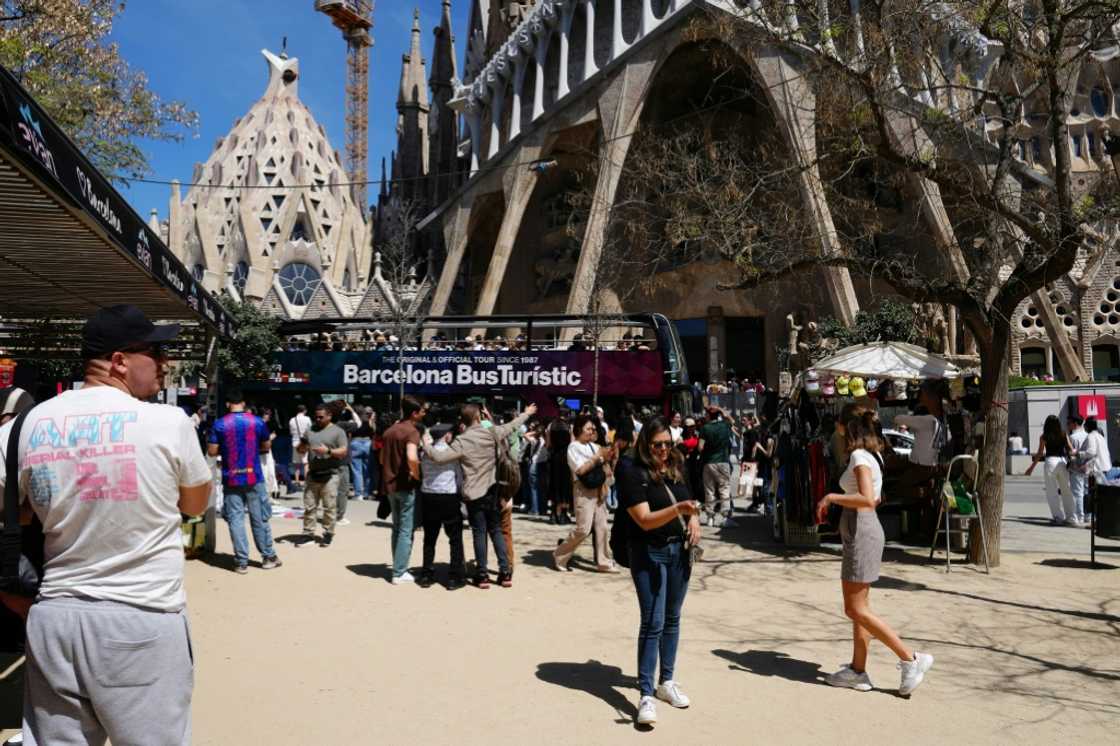 Tourists walk past the Sagrada Familia basilica in Barcelona Tourists walk past the Sagrada Familia basilica in Barcelona