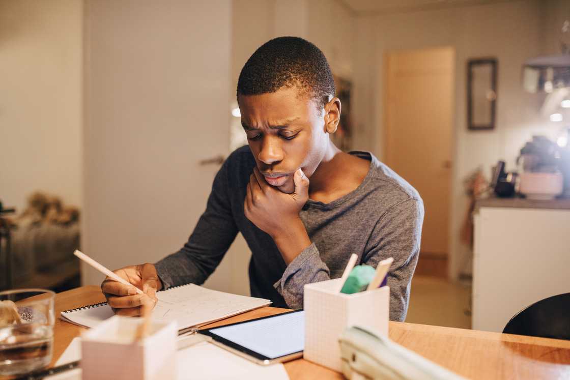 Young person concentrates on homework at a kitchen table.