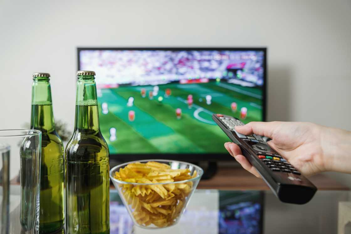 A person holding a remote watching football A person holding a remote watching football