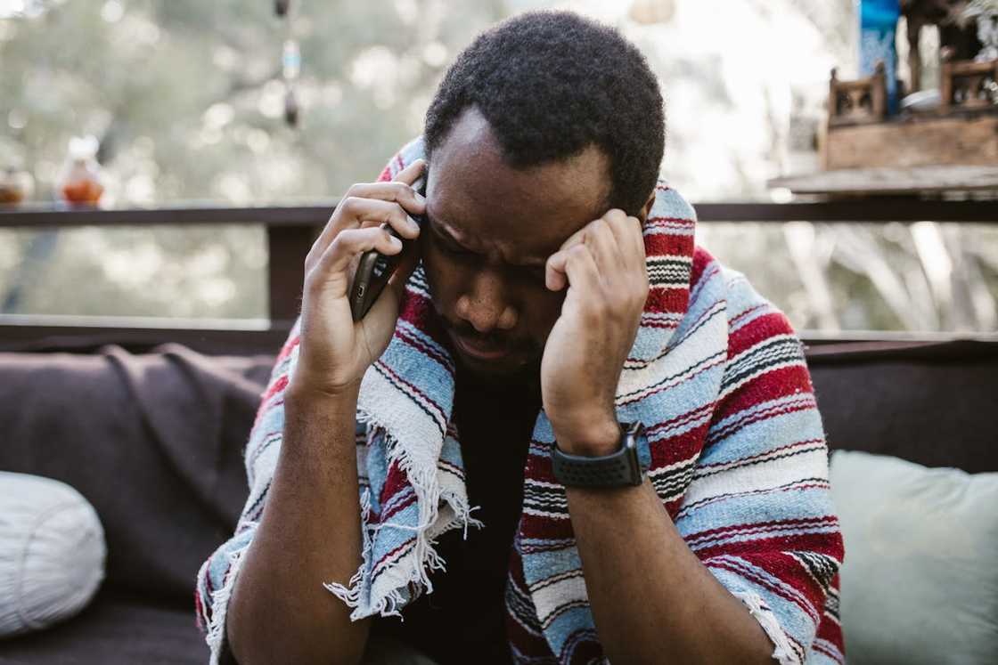 A man on a phone call with his head bowed, appearing stressed.