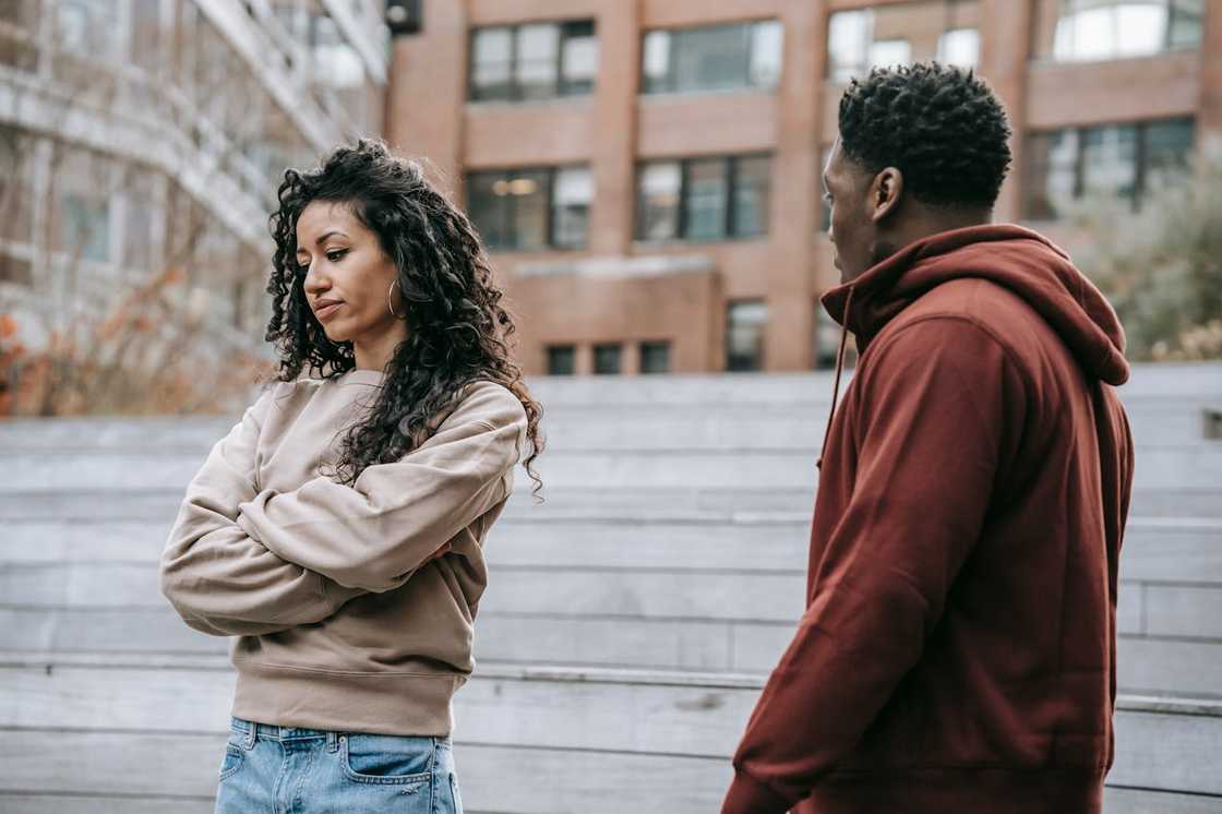 A woman with folded arms faces a man during an outdoor argument.