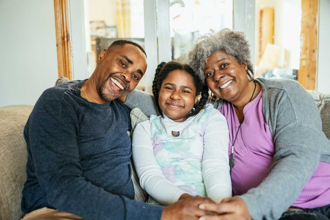 Three people sit close together on a couch, smiling warmly at the camera. Three people sit close together on a couch, smiling warmly at the camera.