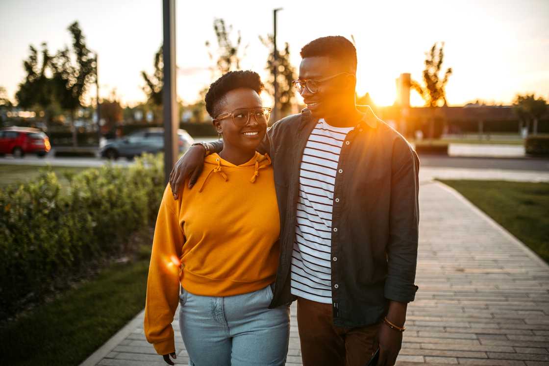 Two people walk together at sunset, one with an arm around the other.