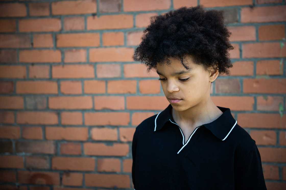 A teenage boy with an afro standing in front of a brick wall A teenage boy with an afro standing in front of a brick wall