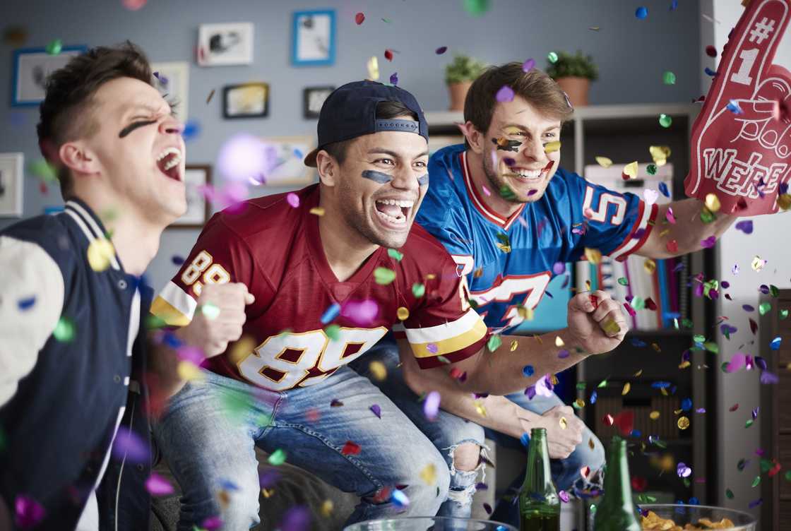 Three American football fans celebrate a win among falling confetti. Three American football fans celebrate a win among falling confetti.