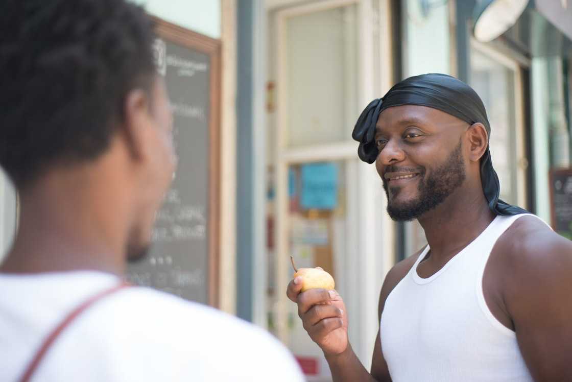A man smiles while holding a pear and talking to another person outdoors. A man smiles while holding a pear and talking to another person outdoors.