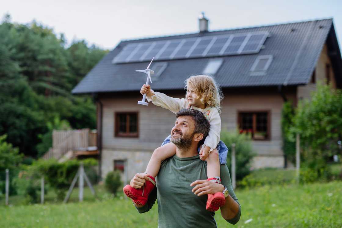 Father carrying his daughter on his shoulders near their family home