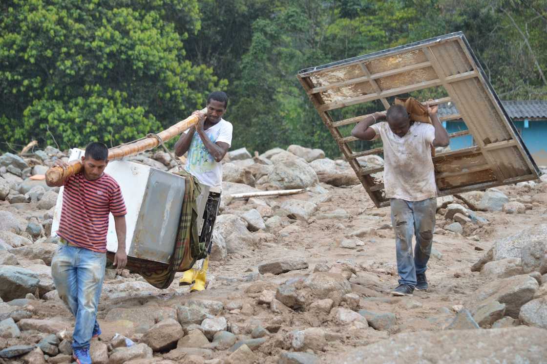 Men carry household debris across muddy ground after flood damage.
