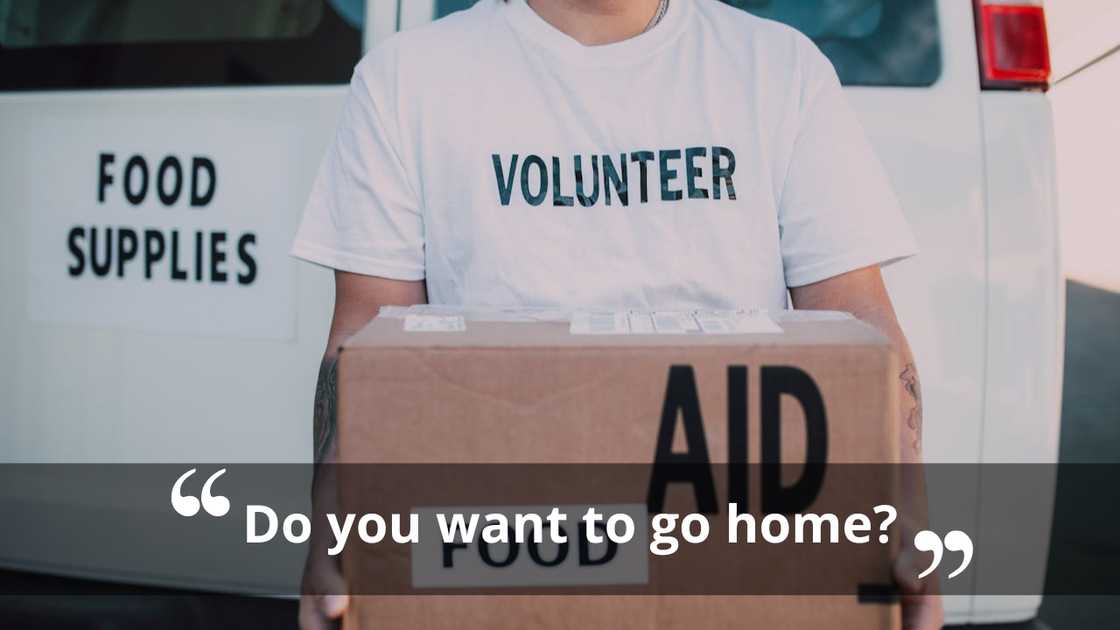 A volunteer holding a box labelled food aid in front of a supply van. A volunteer holding a box labelled food aid in front of a supply van.