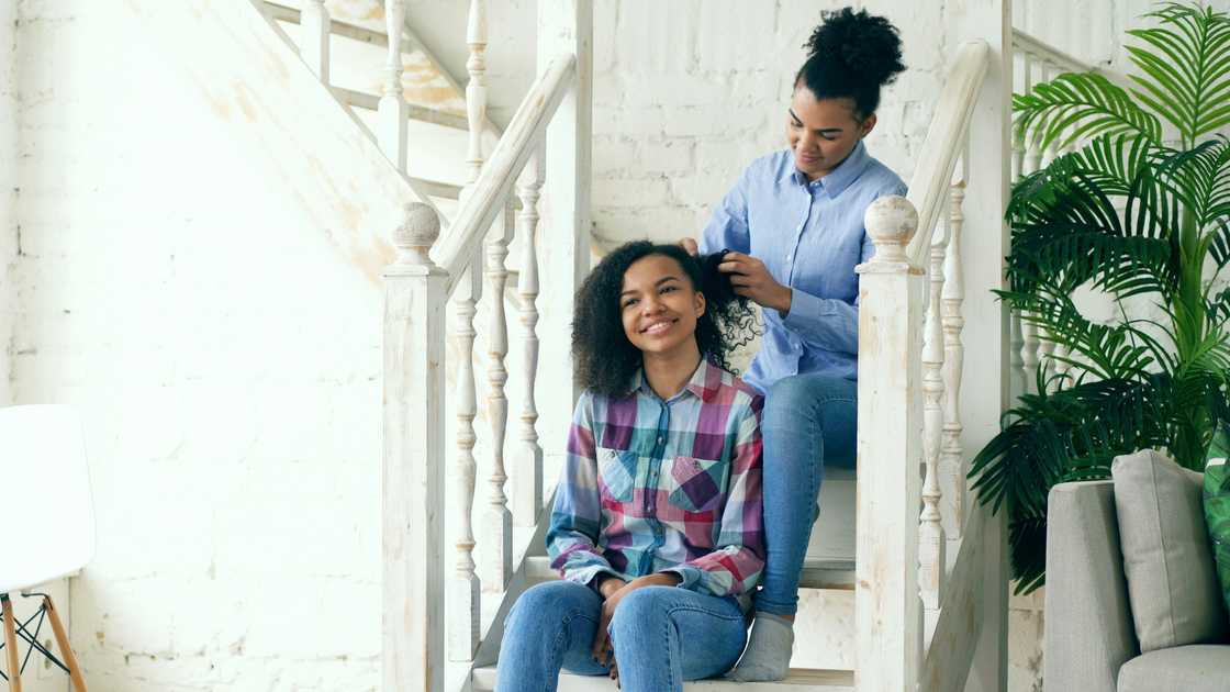 A woman conversing with a teen as she plaits her hair