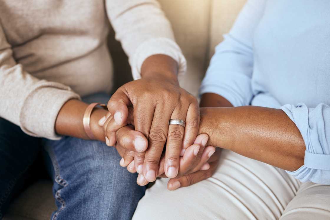 Two people sit side by side, hands gently clasped in a gesture of comfort and connection. Two people sit side by side, hands gently clasped in a gesture of comfort and connection.